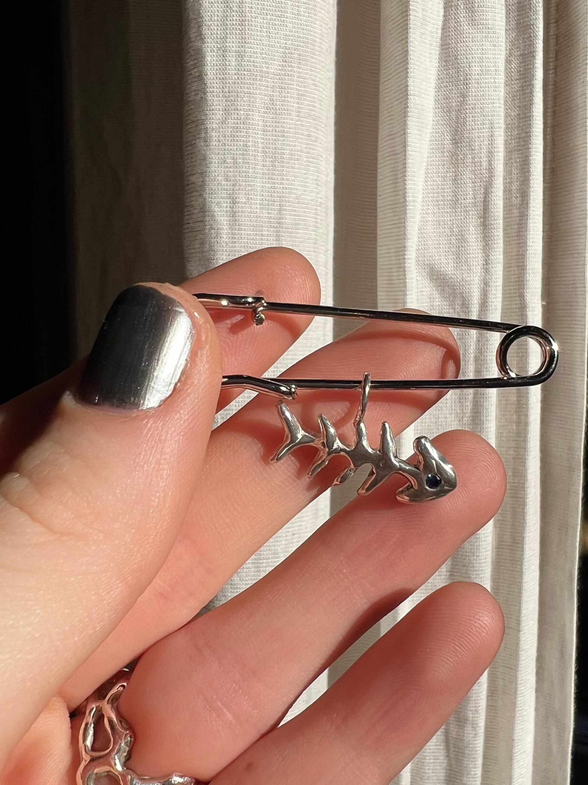Hand holding a large silver safety pin against a neutral background